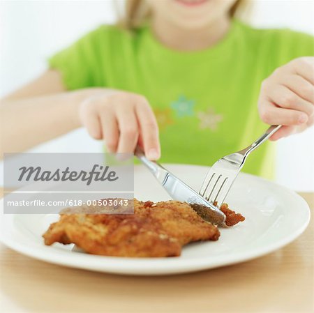 618-00503043em-girl-cutting-a-piece-of-crumb-fried-chicken-with-a-knife-and-fork.jpg